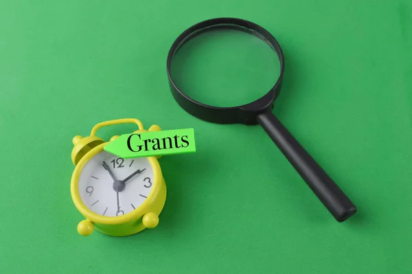 Magnifying glass, clock and memo note with text GRANTS