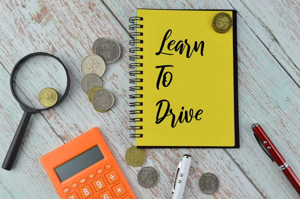 Top view of Pens, coins, calculator, magnifying glass and notebook written with LEARN TO DRIVE.