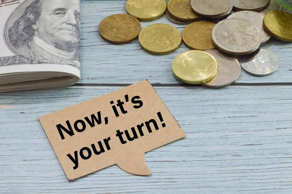 Speech bubble note written with NOW, IT\'S YOUR TURN with coins and money banknotes.