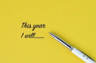 Top view of pen over yellow background written with THIS YEAR I WILL. clipart