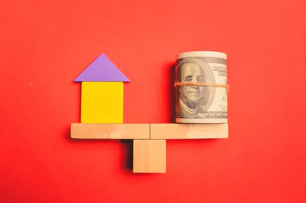Toy wooden house and money banknote isolated on red background. Real estate investment concept.