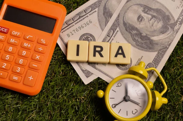 Top view of clock, money banknotes, clock and alphabet letters with text IRA stands for Individual Retirement Account.
