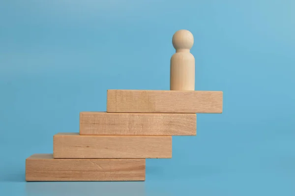 Wooden doll figure standing on wooden blocks.