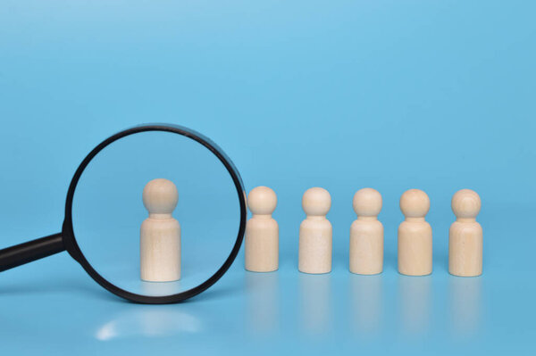 Talent sourcing concept. Wooden doll figures and magnifying glass.