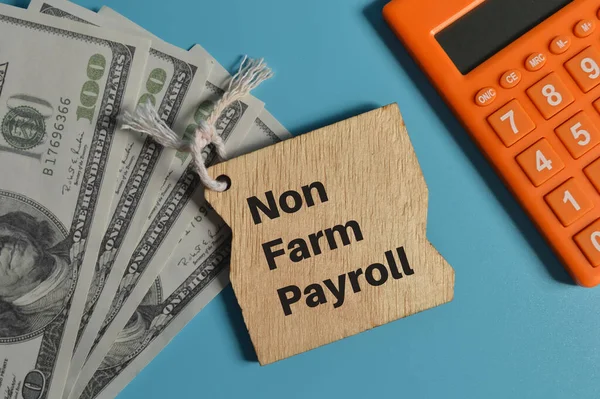 NON FARM PAYROLL ile yazılmış hesap makinesinin üst görünümü, para banknotları ve ahşap tahta.