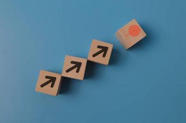 Hedef ve odaklanma konsepti. Tahta blok küpleri yukarı doğru, oklar hedef darta mavi arkaplanda izole edildi.