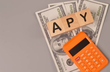 Para banknotları, hesap makinesi ve APY ile yazılmış tahta blokların üst görünümü YILLIK PERCENTAGE YIELD