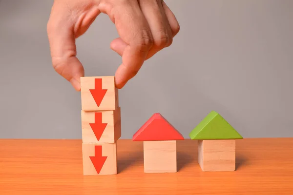 Toy house and red arrow down on wooden blocks. Reducing demand for home buying and low cost real estate concept