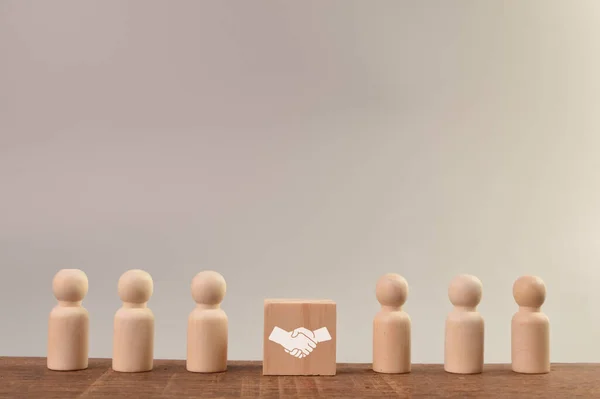 Wooden doll figures and wooden block with handshake icon. Partnership and cooperation concept.