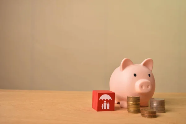 Piggy bank, stack of coins and family symbol on wooden block. Life and family insurance concept