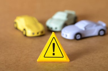 Minyatür arabaların önünde duran sarı uyarı işareti, sürüş tehlikelerini ve yoldaki ihtiyatın önemini simgeliyor..
