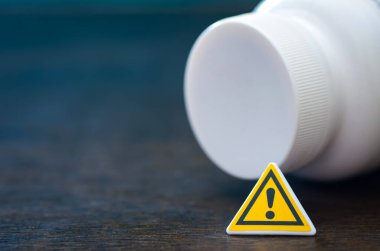 İlaç güvenliği, ilaç riski ve tıbbi kullanımda ihtiyatı sembolize eden uyarı işaretli ilaç şişesi.