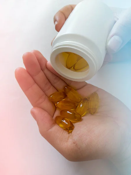 Beyaz arka planda vitaminler. Kavanozdan hap al. Sarı kasuli ellerinde.