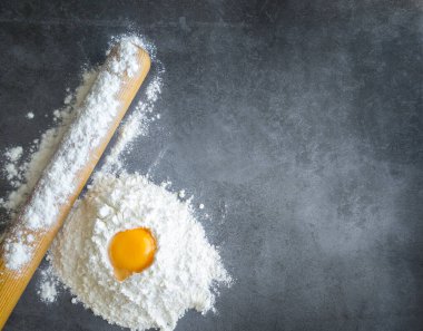 Sol alt köşedeki un içinde çiğ yumurta. Koyu bir arka planda yuvarlak iğne ve un. Boş alan