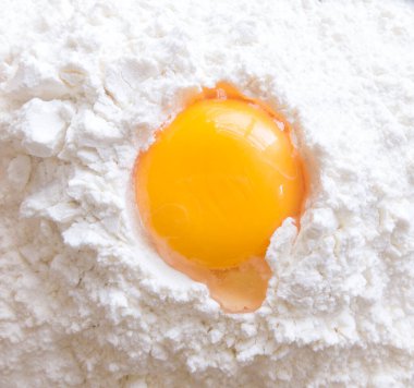 Kırık yumurta unun içinde yatıyor. Un arkaplanındaki büyük çiğ yumurta sarısının fotoğrafı.