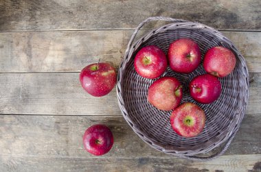 Tepside ve masada kırmızı elmalar. Eski ahşap arka planda meyveler. Kaliteli bir yüzey üzerinde yemek olan hasır kaplar..