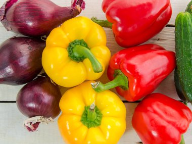 Dolmalık biber, kırmızı soğan, beyaz ahşap bir masada salatalık. Salata için doğal malzemeler. Vejetaryen, sağlıklı yemek. Yaz hasadı.