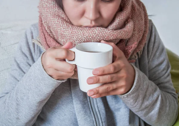 A young woman has a cold and drinks medicine. Autumn is the time of colds. The girl her throat with a scarf and drank hot. Treatment with folk remedies. On a winter evening, warm up with hot cocoa.