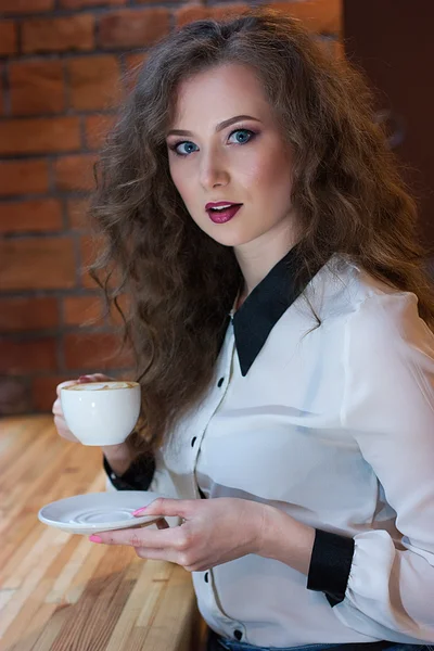 Удивлённая девушка с кофе у кирпичной стены — стоковое фото
