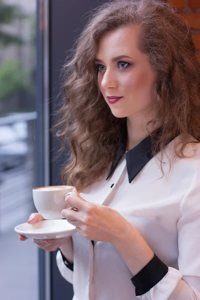 Όμορφη κοπέλα με καφέ σε ένα λευκό πουκάμισο στο παράθυρο — Φωτογραφία Αρχείου