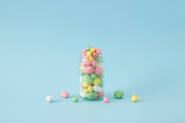 Pastel rengi pembe, sarı, yeşil ve beyaz bıldırcın yumurtaları cam kavanozda. Mavi arkaplanda yaratıcı bir kavram.