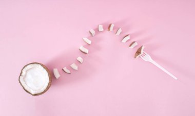 Beyaz çatallı taze, organik hindistan cevizi yeme fikri. Hindistan cevizi tabağından küçük hindistan cevizi parçaları geliyor. Meyve konsepti, pastel pembe arka planda düz uzanma.