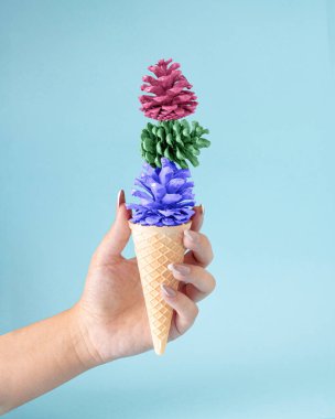 Pastel renginde, elinde kozalakla yapılan sonbahar dondurması. Yaz sonu için lezzetli bir şeker. Pastel mavi arkaplan üzerine yaratıcı kavram.