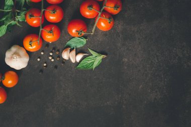 Üzüm domatesleri, fesleğen yaprağı, sarımsak karanfilleri ve karabiber ile pişirmek için çeşitli baharatların üst masa görünümü ayrıca siyah paslı masa zemininde beyaz biber..