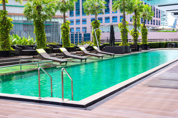 Relaxing pool bed or sofa arrange beside green swimming pool and building in the city in background.