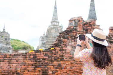 Dikiz manzaralı, cerrahi maske takan Asyalı kadın turist, tarihi parkta eski başkent pagoda 'sı ya da aptalca bir geçmişi olan fotoğraflar çekiyor. Covid-19 salgını sırasında seyahat etmek ve yeni normal kavram.