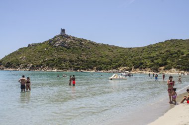Kimliği belirsiz kişi Beach Porto Giunco (Villasimius). Güneşli bir günde insanlar Beach, şeffaf deniz ile yaz ve Dağı'nda tarihi Kulesi