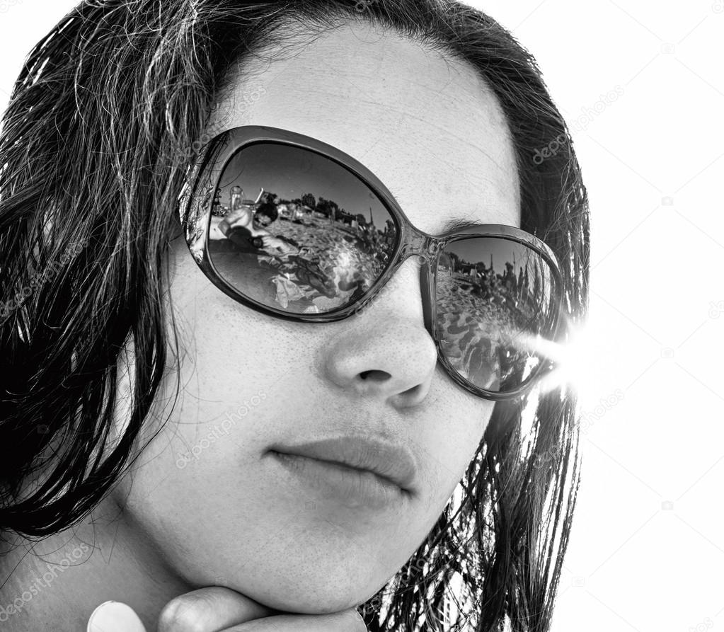 Face of young brunette girl in sunglasses with beach reflection in bright sun rays black and white HDR effect