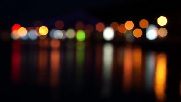 Θολή φώτα της πόλης τη νύχτα με αντανακλάσεις στο νερό — Αρχείο Βίντεο