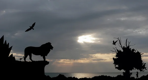 Dschungel mit Bergen, altem Baum, Vögeln Löwe und Erdmännchen am Meer Sonnenuntergang mit grauem bewölkten Himmel Hintergrund — Stockfoto