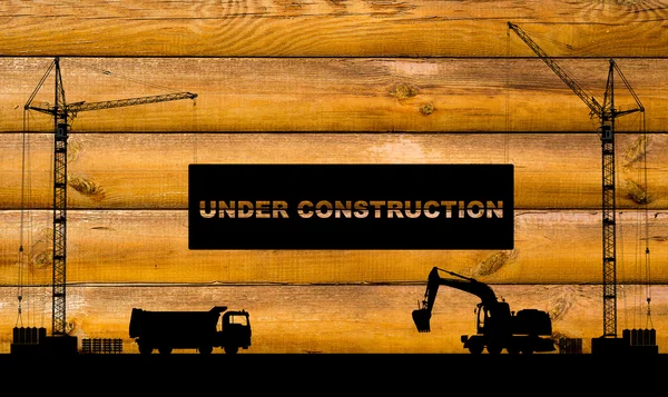 "Under construction" concept at building site with detailed silhouettes of construction machines on beech wood texture background — Stock Photo, Image