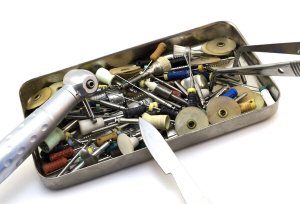 Набор стоматологических инструментов: резаки, иглы, сверла, скальпель, щипцы в металлической коробке, изолированной на белом
