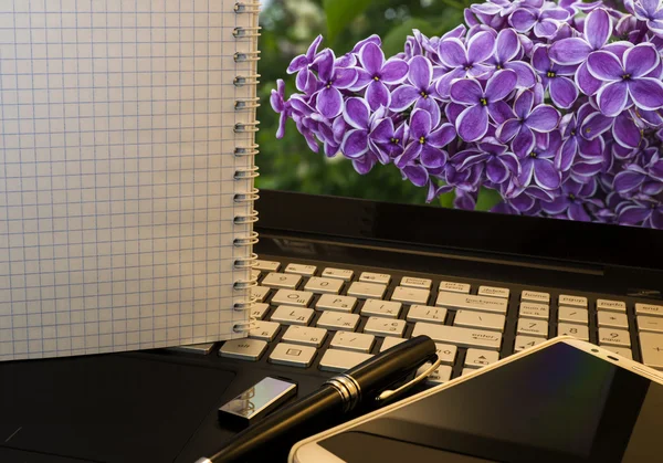 Bureau avec ordinateur portable, téléphone intelligent, stylo, lecteur flash et wordpad avec fond de fleurs violettes — Photo