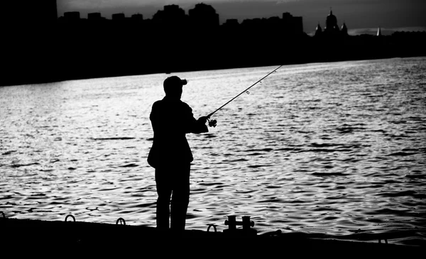 Pêcheur debout sur le bord du quai avec canne à pêche près de la rivière en ville noir et blanc — Photo