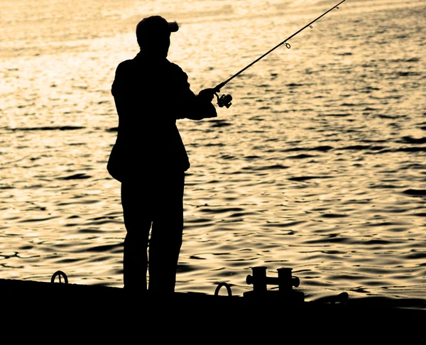 Pescador de pie en el borde del muelle con caña de pescar cerca del río en la ciudad caliente filtrado — Foto de Stock