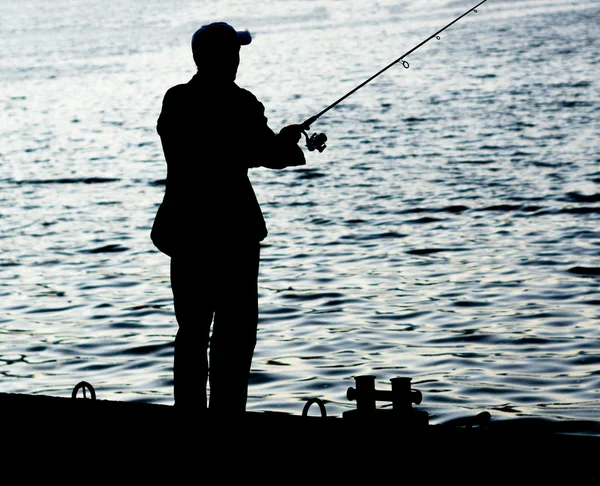 Fisherman standing on edge of dock with fishing rod near river in city — Stock Photo, Image