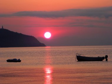 Kayalar ve tekne ile denizde kırmızı günbatımı