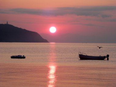 Deniz kaya, tekneler ve martı ile üzerinde kırmızı günbatımı