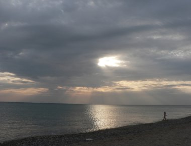 Sunset Bulvarında gri bulutlu gökyüzü, çalışan çocuk, ışınları ışık ve Plajı ile deniz