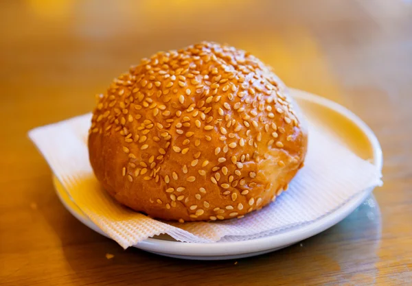 Golden fresh bun with sesame seeds on white plate with napkin — Stock Photo, Image