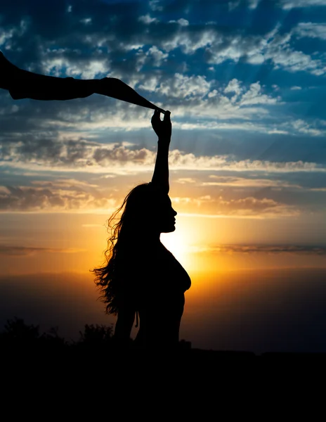 Silhouette de jeune fille avec châle sur fond de beau ciel bleu nuageux avec coucher de soleil jaune doré et rayons de lumière — Photo