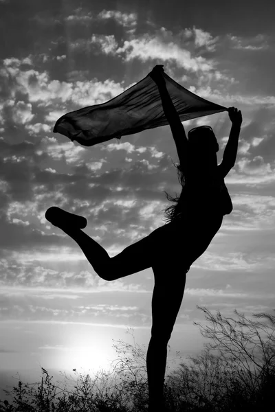 Silueta de niña con chal bailando sobre fondo de hermoso cielo nublado con puesta de sol y rayos de luz en blanco y negro —  Fotos de Stock