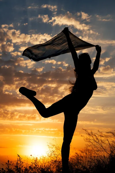 Silueta de niña con chal bailando sobre fondo de hermoso cielo nublado con puesta de sol naranja y rayos de luz —  Fotos de Stock