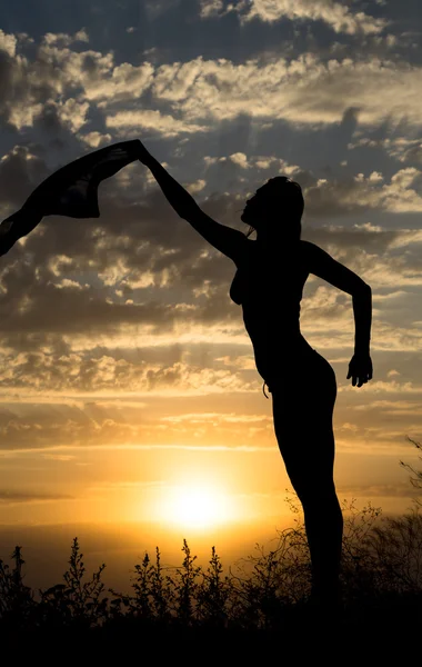 Silhouette de jeune fille avec châle sur fond de beau ciel bleu nuageux avec coucher de soleil jaune doré et rayons de lumière — Photo