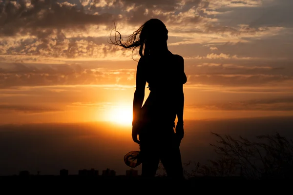 Fiatal lány sziluettje kendőt a háttérben a gyönyörű felhős ég, az arany-vörös naplemente és fénysugarak — Stock Fotó