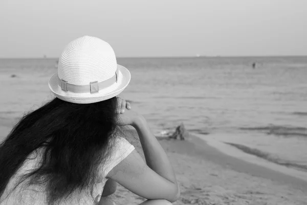 Lány barna-fehér kalapot keres a tengeren ülve beach fekete-fehér — Stock Fotó